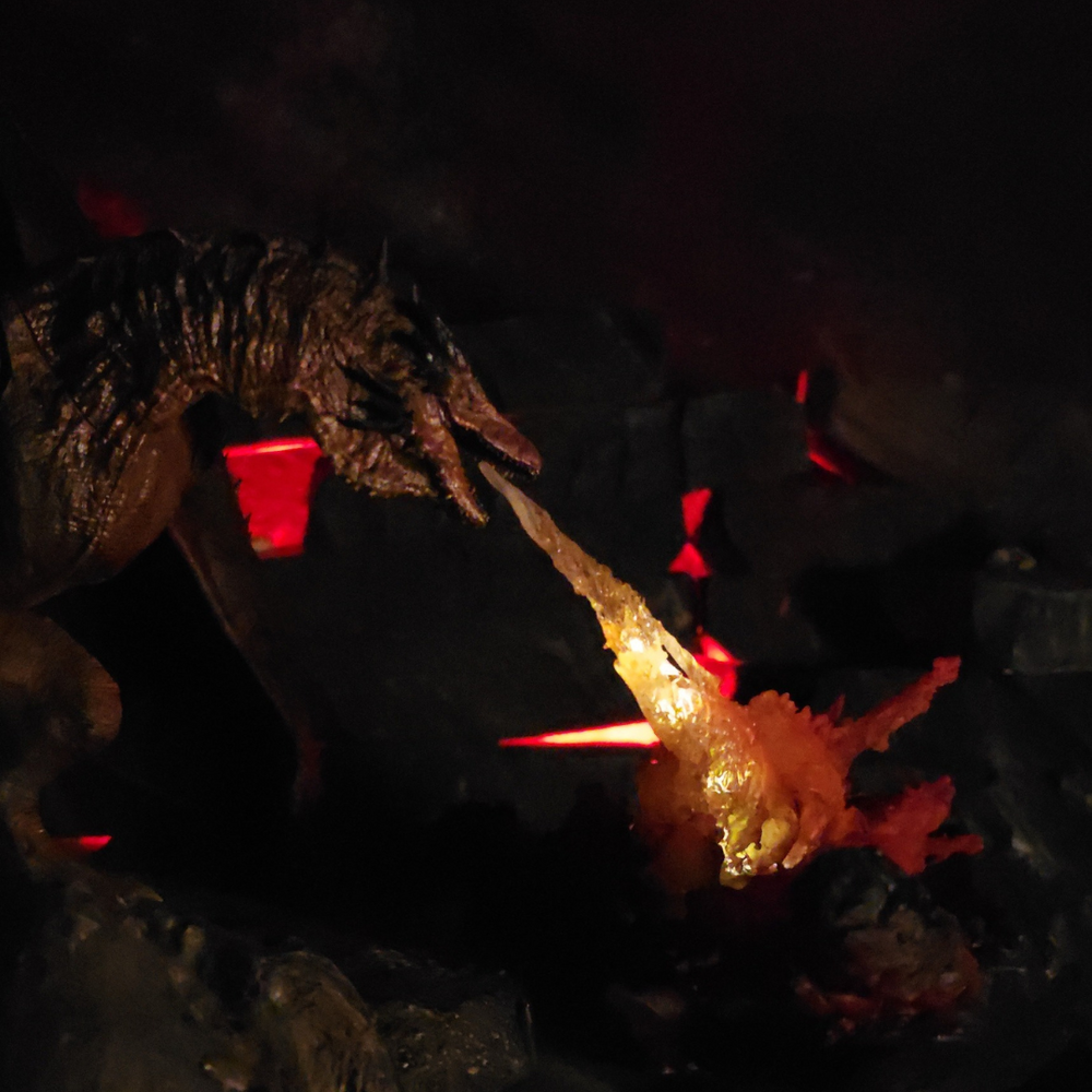 
                  
                    Silhouette du dragon Bronze Fury dans l’obscurité, projetant un souffle lumineux sur un champ de lave.
                  
                
