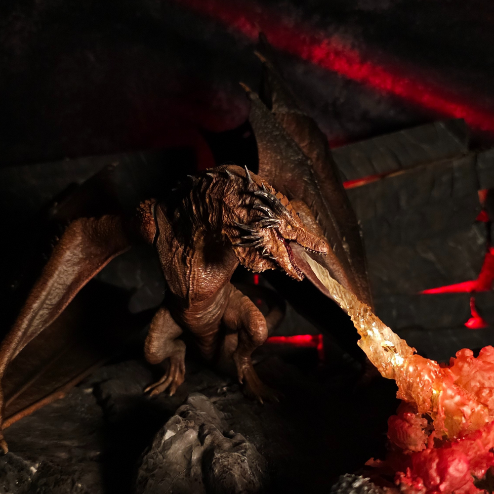 
                  
                    Figurine du dragon Bronze Fury crachant des flammes sur un sol volcanique, dans une scène inspirée de l’univers de House of the Dragon.
                  
                
